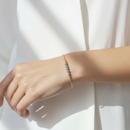A woman wearing a Me19 micro gold-plated bracelet. The bracelet features a fine chain with grey/blue faceted beads and small gold beads. A minimalist and elegant piece of artificial jewellery from Kerala, India