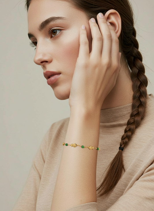 A woman wearing a Me19 micro gold-plated bracelet with alternating fish motifs and green beads. A delicate and elegant piece of artificial jewellery from Kerala, India